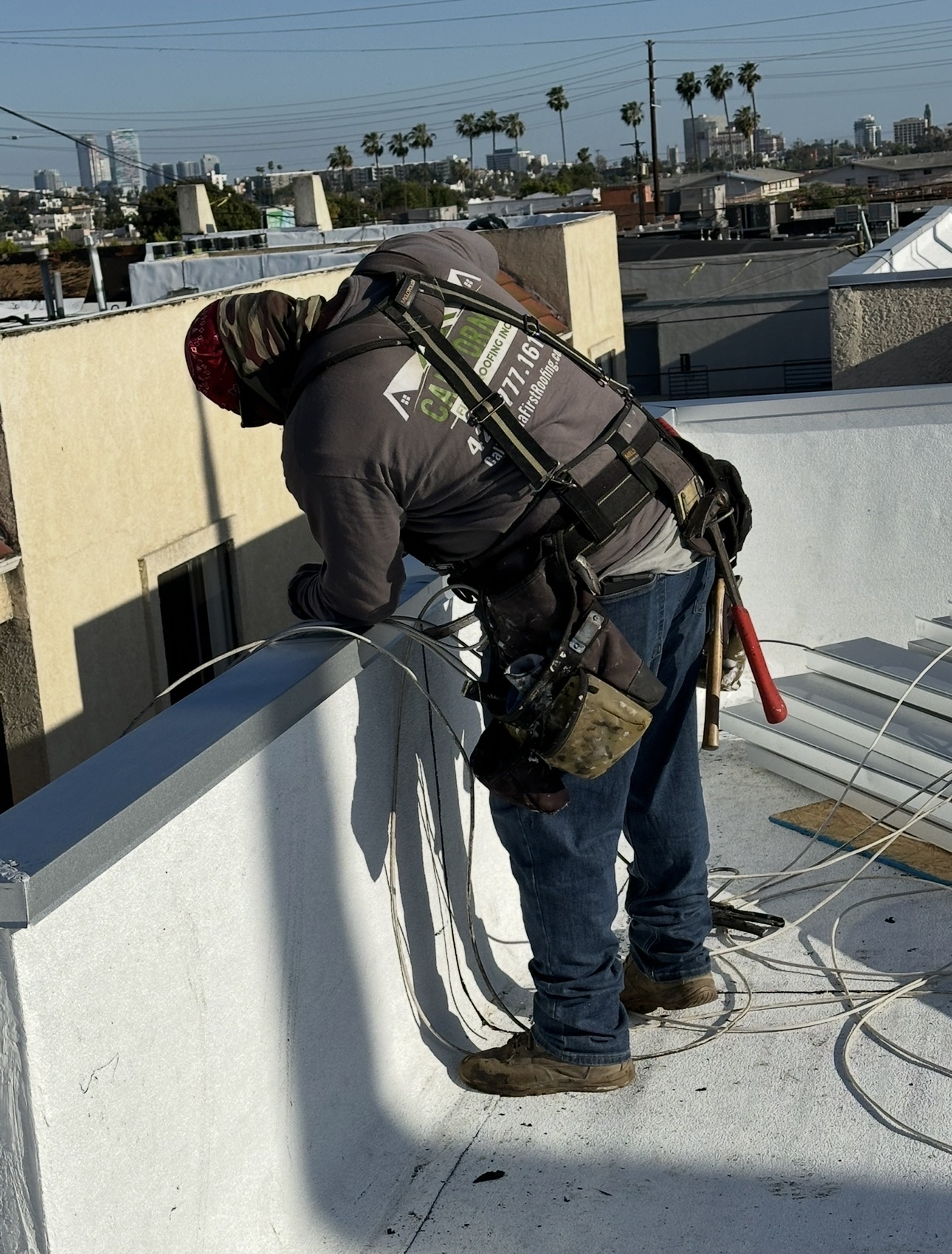 Roofer finishing parapet coating on a Hollywood flat roof with city skyline