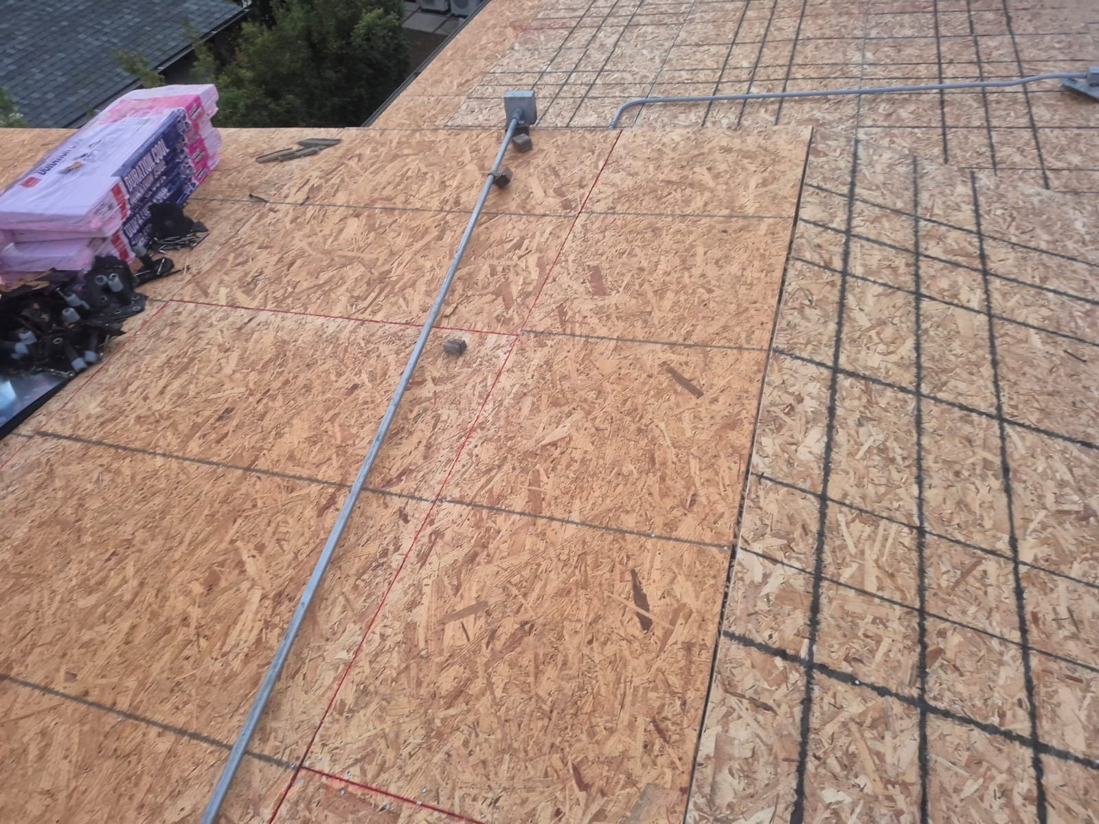 Fresh OSB decking with underlayment lines and staged shingle bundles